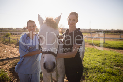 Portrait of smiling jockey and vet standing by horse at barn