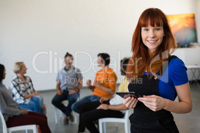 Portrait of happy teacher holding digital tablet with students talking in background