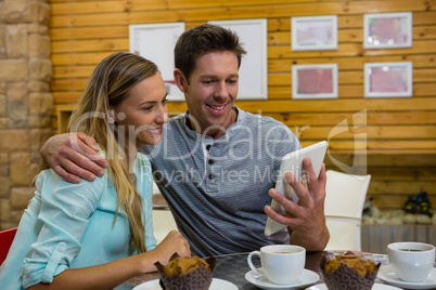 Man showing digital tablet to girlfriend in coffee shop