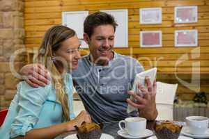 Man showing digital tablet to girlfriend in coffee shop