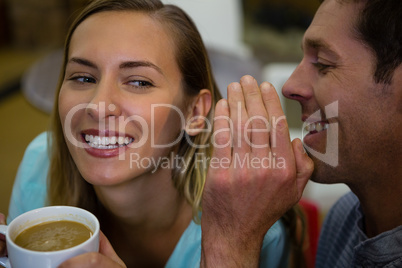 Happy man whispering into ears of girlfriend having coffee