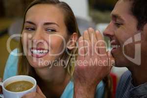 Happy man whispering into ears of girlfriend having coffee