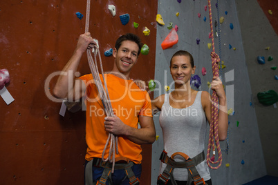 Portrait of athlete holding rope while standing by climbing wall at gym
