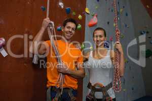 Portrait of athlete holding rope while standing by climbing wall at gym