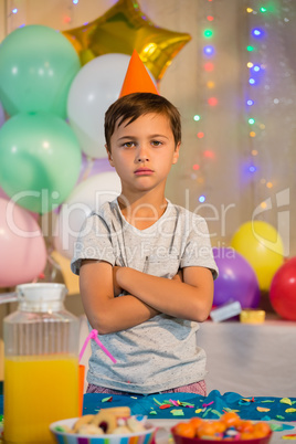 Cute boy standing with arms crossed at birthday party