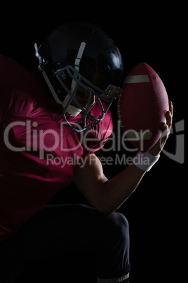 American football player sitting holding a ball in his hand