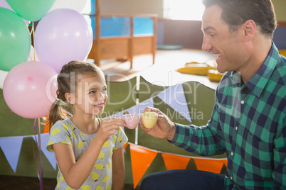 Father and girl toasting their tea cups while playing with toy kitchen set