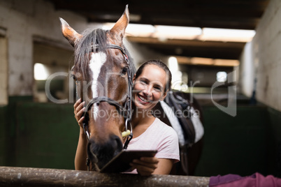 Portrait of female jockey holding tablet computer while standing by horse