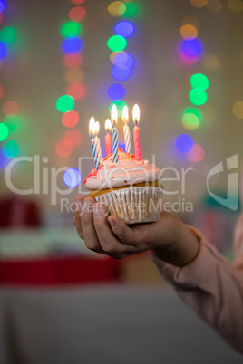 Girl holding cupcake with lit candle during birthday party