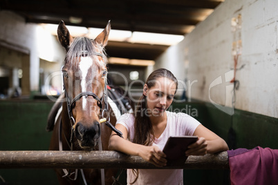 Female jockey using tablet computer while standing against horse