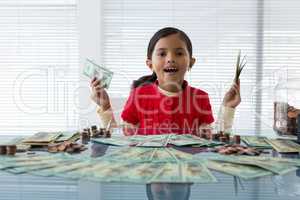 Portrait of girl holding currency while sitting at desk