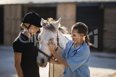 Female jockey looking at vet stroking horse