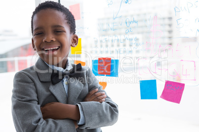 Portrait of happy businessman with arms crossed standing by window at office