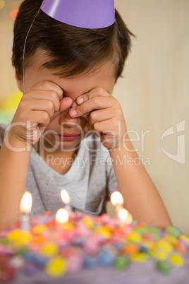 Upset boy sitting in front of birthday cake