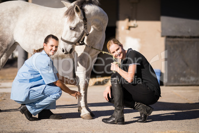 Portrait of female jockey and vet crouching by horse