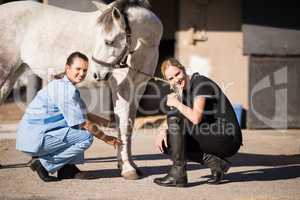 Portrait of female jockey and vet crouching by horse
