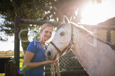 Smiling young woman standing by horse at barn