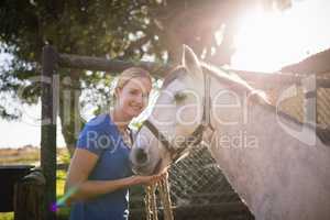 Smiling young woman standing by horse at barn