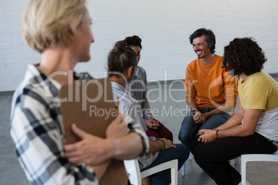 Female teacher looking at students talking while sitting on chair