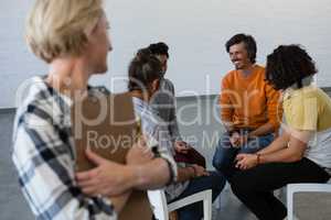 Female teacher looking at students talking while sitting on chair