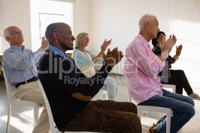 Smiling senior people applauding while sitting on chair