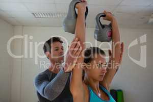 Trainer assisting female athlete in lifting kettlebells