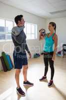 Full length of trainer with female athlete lifting kettlebells