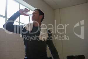 Athlete drinking water while standing in gym