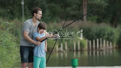 Father teaching son to fish at lakeside in summer