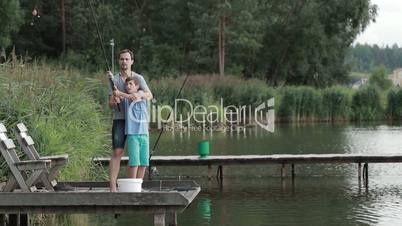 Father teaching son to cast fishing rod on lake