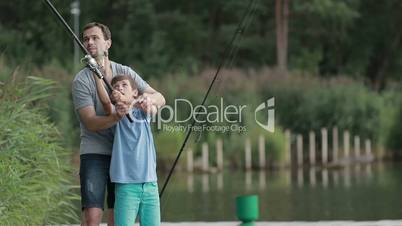 Teenage boy learning to fish with father's help