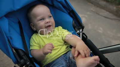 Funny little infant boy in baby stroller in park