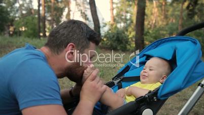 Loving father kissing feet of his baby son in park