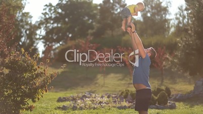 Playful dad throwing baby boy high in summer park