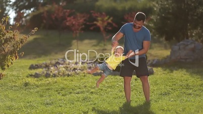 Cheerful father swinging his baby boy in park