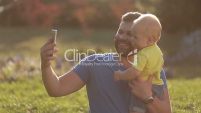 Smiling father and baby son making selfie in park