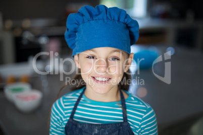 Smiling girl wearing an apron and a cap in the kitchen