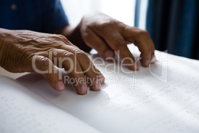 Cropped hands on retired man reading braille book in retirement home
