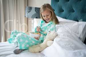 Smiling girl feeding breakfast to teady bear on bed