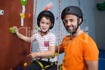 Trainer assisting boy in rock climbing at fitness studio