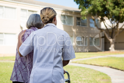 Rear view of doctor assisting senior woman in walking