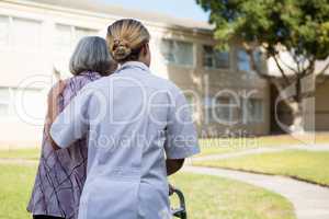 Rear view of doctor assisting senior woman in walking
