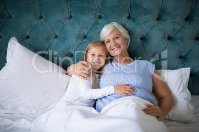 Smiling granddaughter and grandmother sitting together on bed