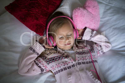 Girl listening to music on headphones while lying on bed