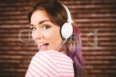 Woman listening music on headphones against brick wall
