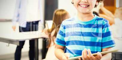 Portrait of smilng schoolboy holding digital tablet in classroom