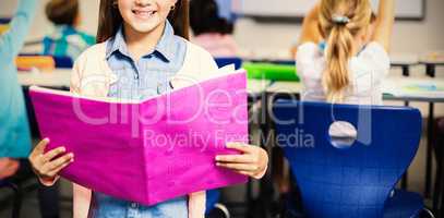 Portrait of schoolgirl with book standing in classroom