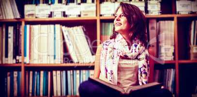 Thoughtful female student against bookshelf on library floor