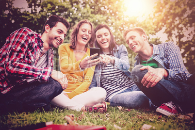 Cheerful college students looking at mobile phone while sitting together