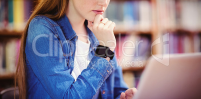 Student with smartwatch using laptop in library